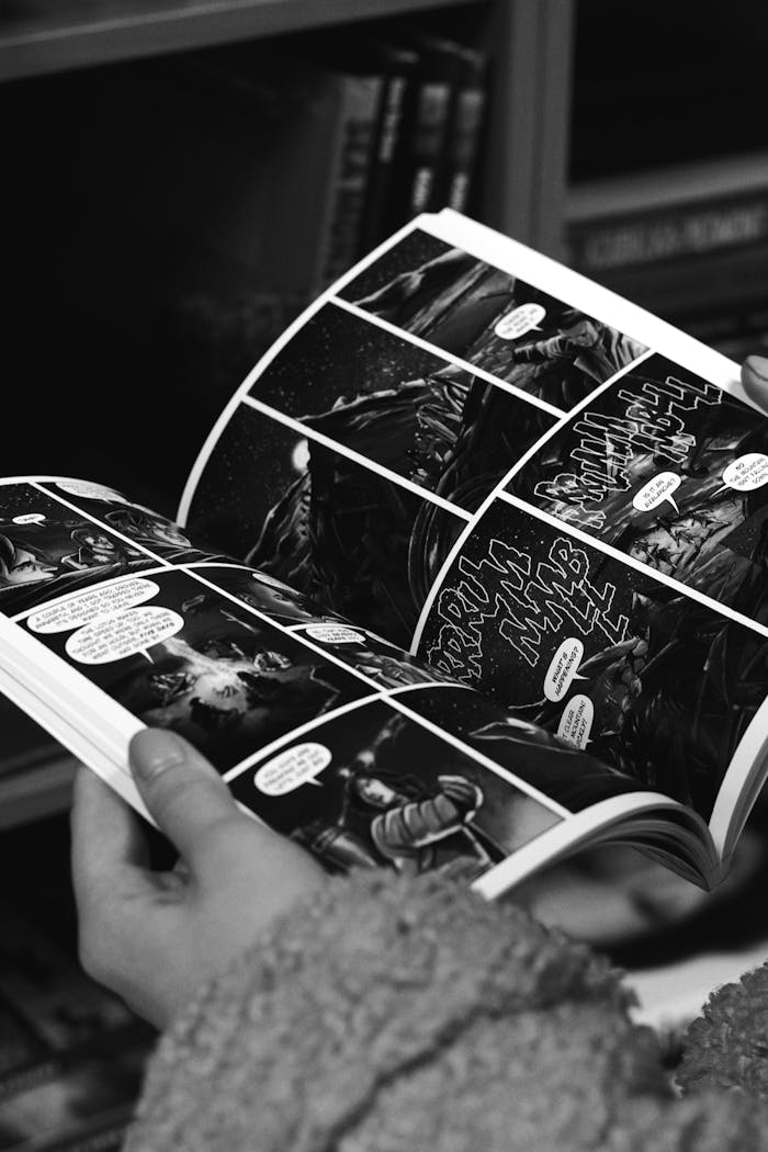 Black and white photo of a person reading a comic book, capturing detailed artwork.